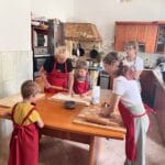 Dwie panie z dziećmi podczas lepienia pierogów w kuchni